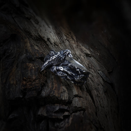Close-up of sterling silver ring showcasing detailed raven design, set against a rustic wood background.