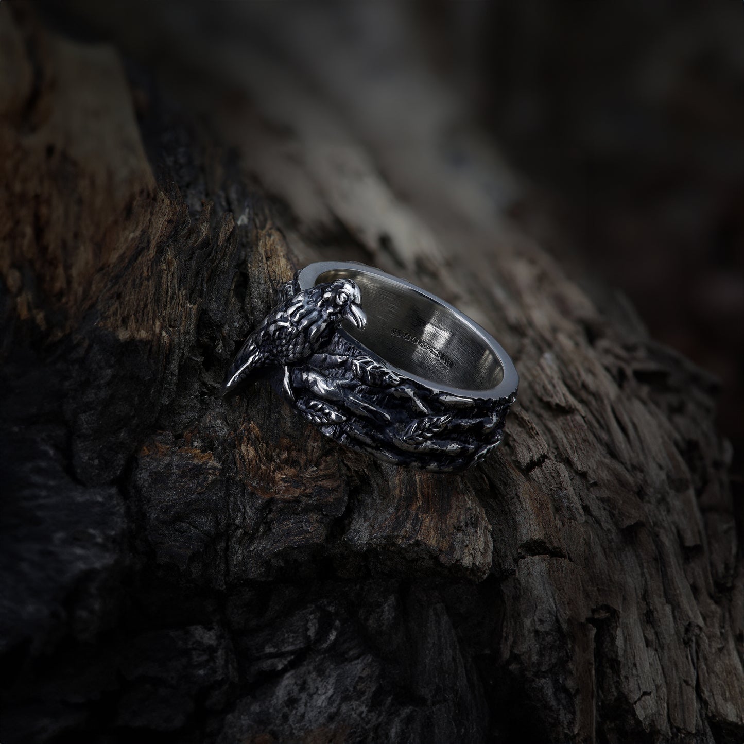 Side profile of sterling silver ring highlighting the depth of the raven and twig design on wood.