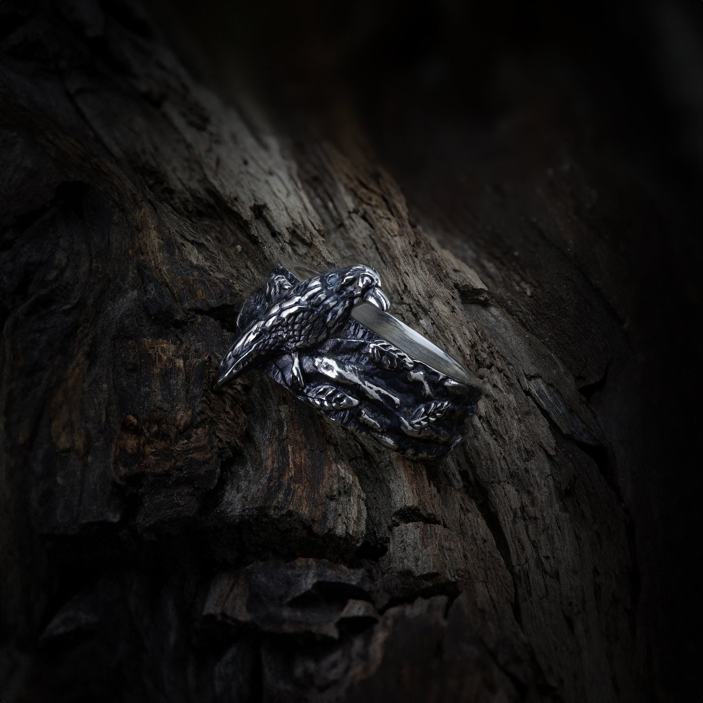 Close-up of sterling silver ring showcasing detailed raven design, set against a rustic wood background.