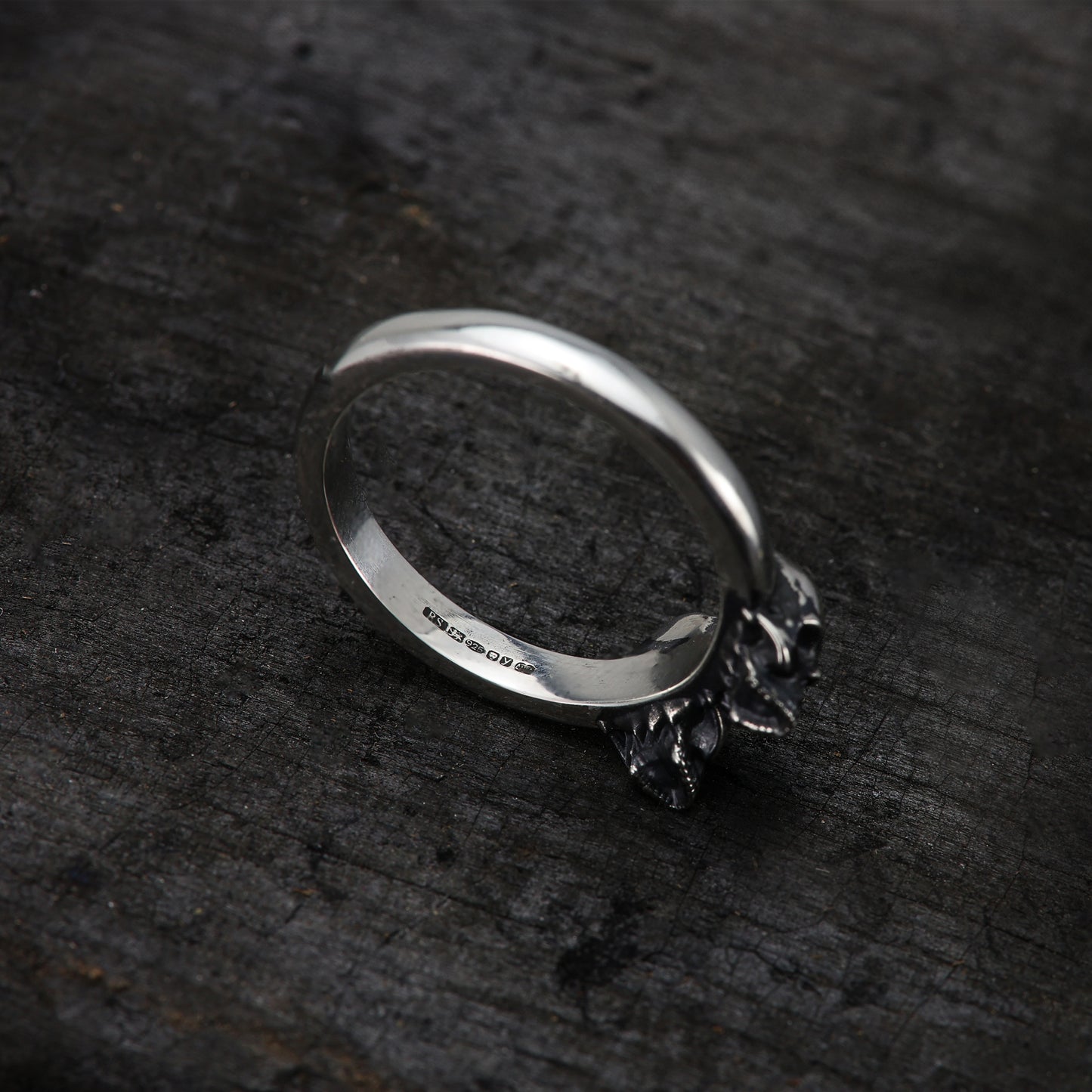 Person wearing sterling silver double skull band on finger, showcasing hallmark.