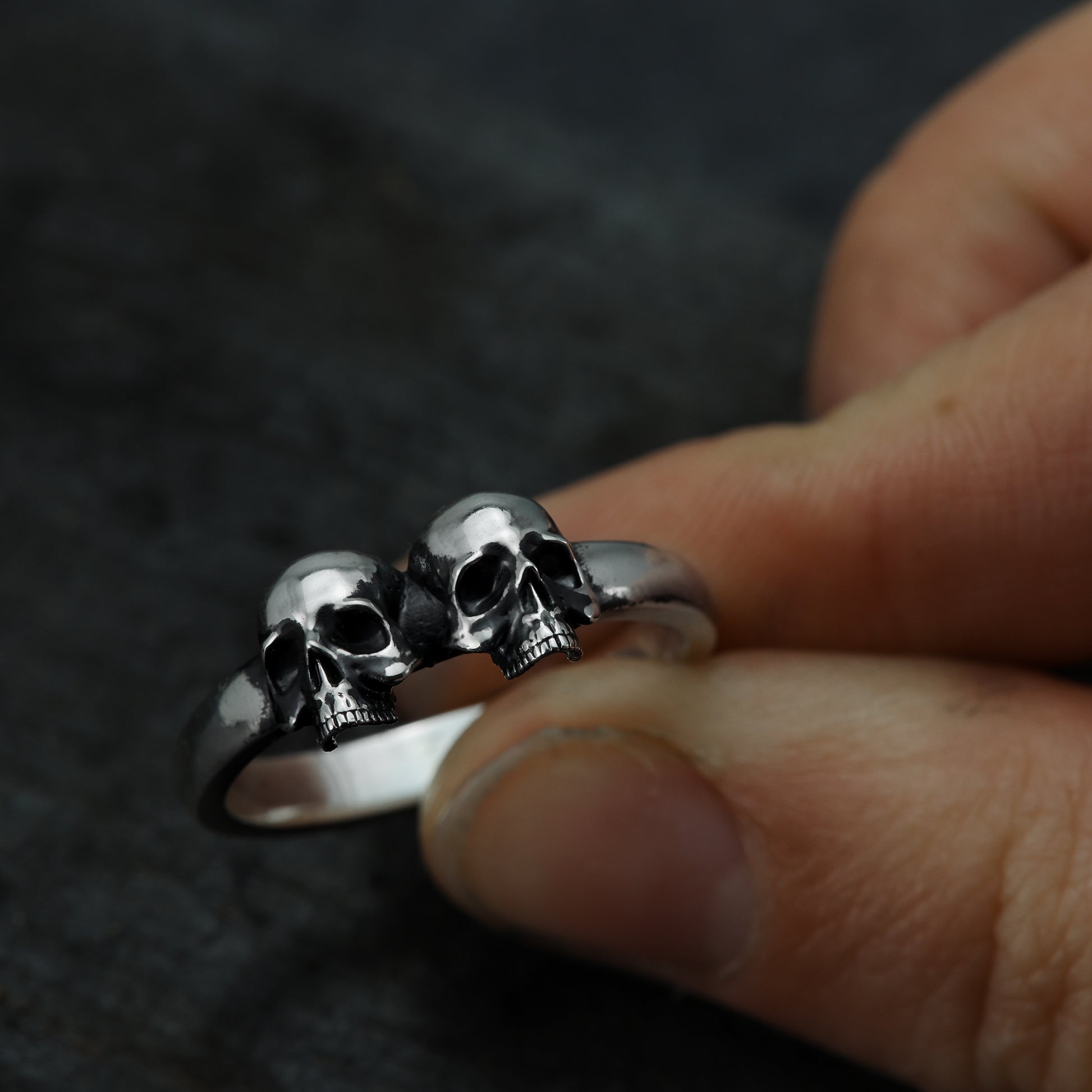 Hand holding sterling silver double skull ring.