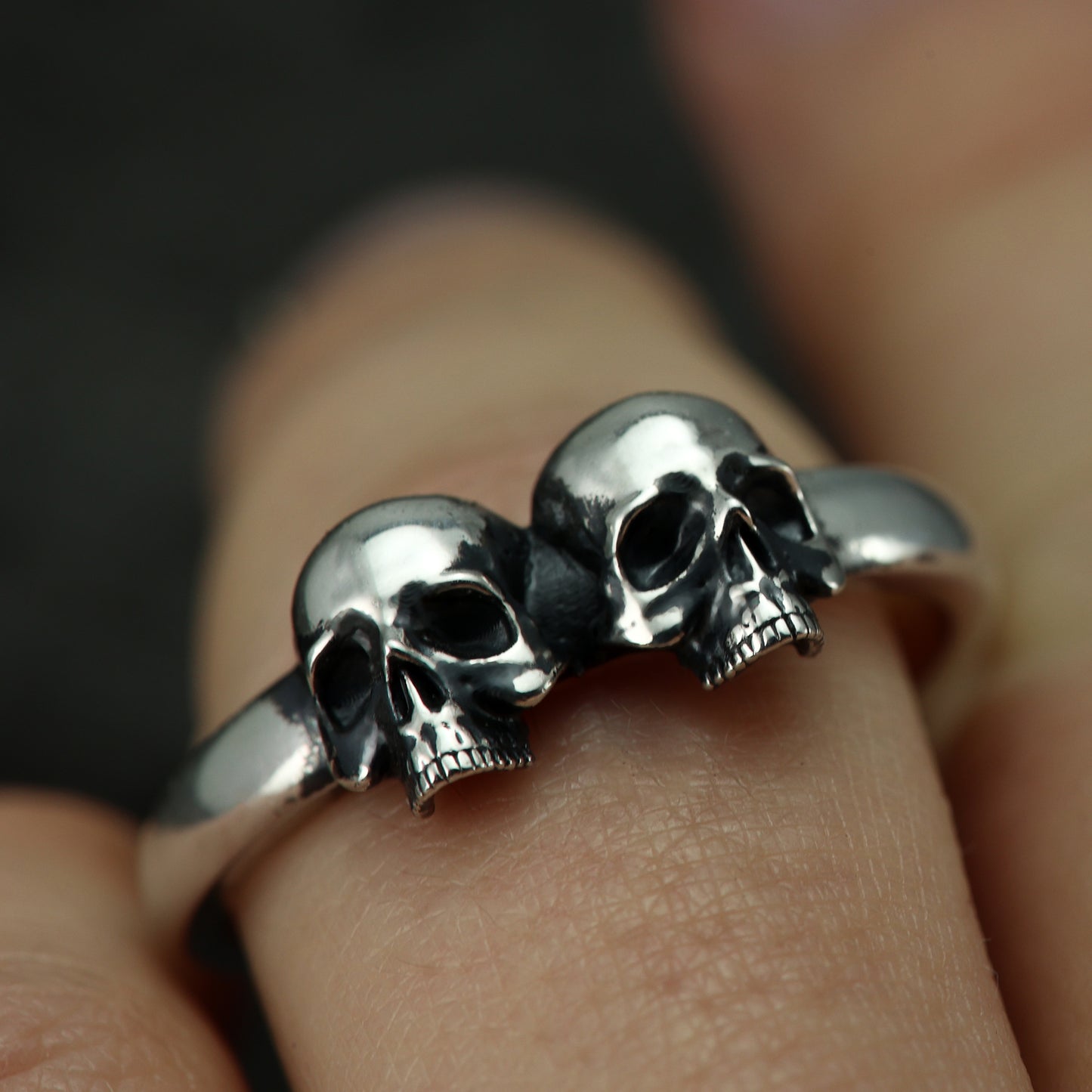 Person wearing sterling silver double skull band on finger.