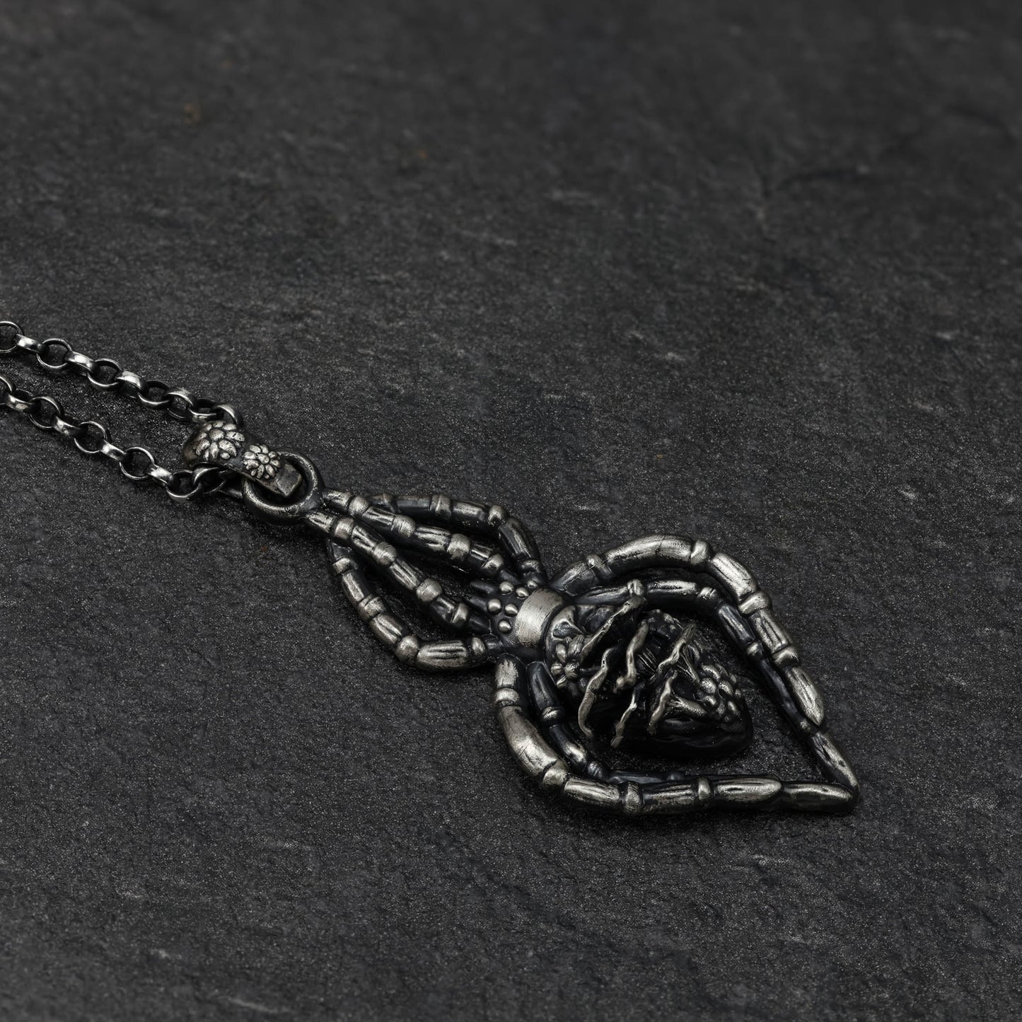 A close-up of a highly detailed sterling silver spider necklace with tiny flowers and mushrooms..