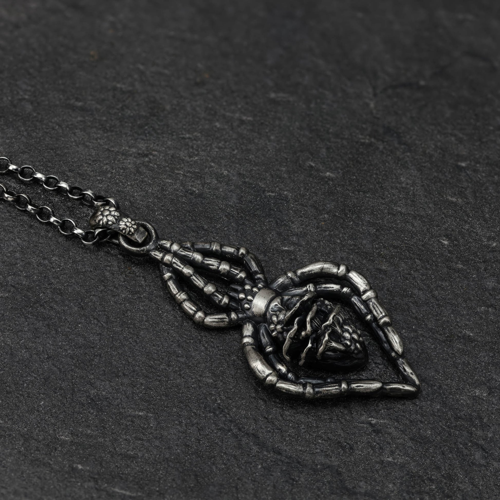 A close-up of a highly detailed sterling silver spider necklace with tiny flowers and mushrooms..